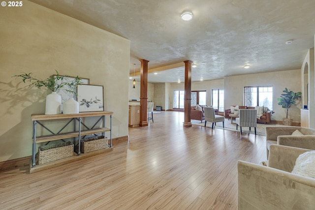 interior space with light wood-type flooring, ornate columns, and baseboards