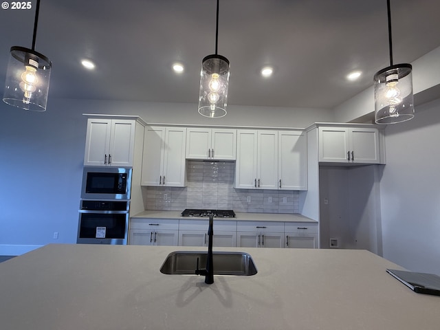 kitchen featuring stainless steel appliances, light countertops, backsplash, white cabinets, and a sink