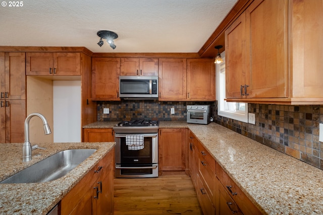 14424 SE Bevington Ct, Milwaukie, OR 97267 - kitchen featuring stainless steel appliances, brown cabinets, light wood-style flooring, decorative backsplash, and a textured ceiling