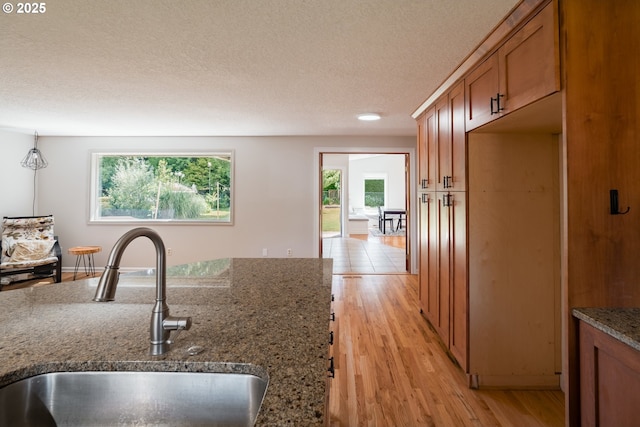 14424 SE Bevington Ct, Milwaukie, OR 97267 - kitchen featuring brown cabinetry, light wood-style flooring, a textured ceiling, and stone countertops