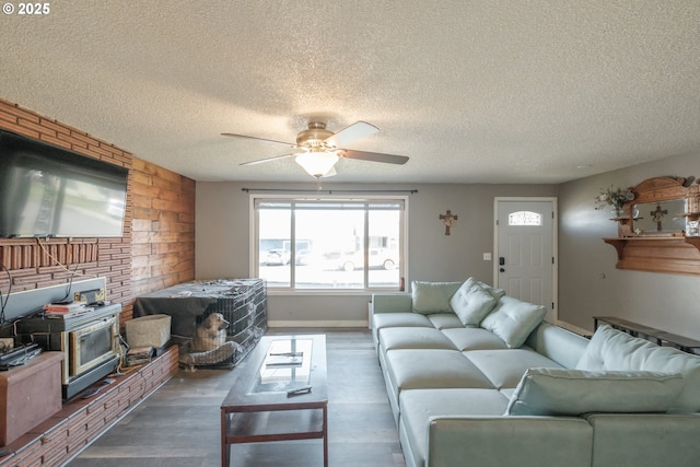 living room with a textured ceiling, wood finished floors, a wood stove, and a ceiling fan