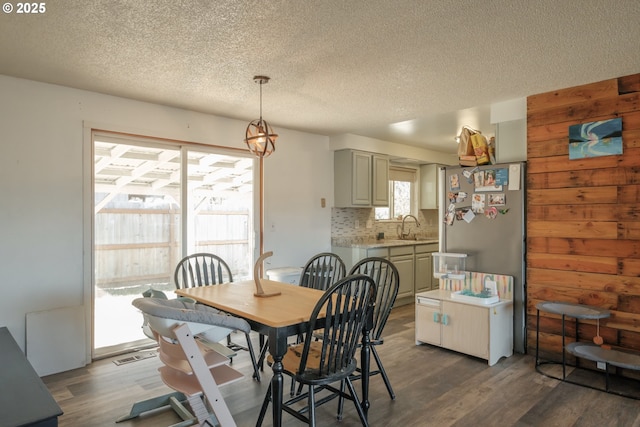 dining space with a textured ceiling, dark wood-type flooring, visible vents, and wooden walls