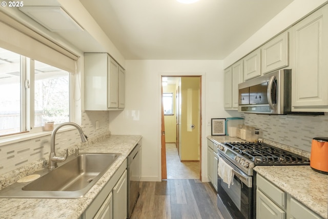 kitchen featuring appliances with stainless steel finishes, wood finished floors, a sink, light countertops, and backsplash