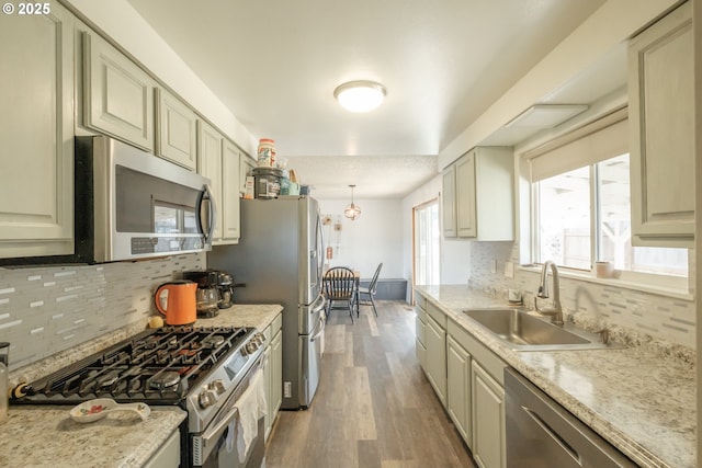 kitchen with stainless steel appliances, a sink, decorative backsplash, dark wood finished floors, and pendant lighting