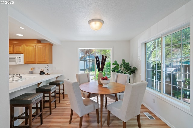 dining space featuring baseboards, light wood-type flooring, a textured ceiling, and visible vents
