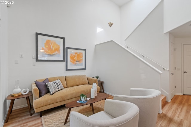 living room featuring stairway, baseboards, a high ceiling, and light wood-style flooring