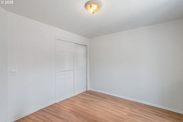 unfurnished bedroom featuring baseboards, a closet, and light wood-type flooring