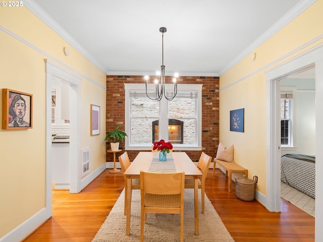 2127 NW Irving St Unit 104, Portland, OR 97210 - dining room with light wood finished floors, a chandelier, baseboards, ornamental molding, and brick wall