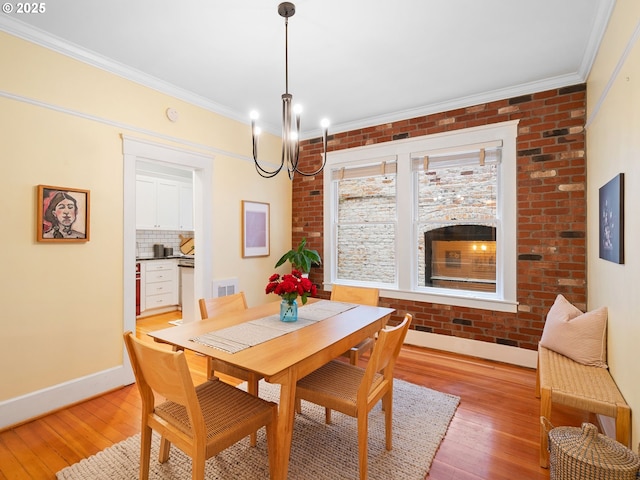2127 NW Irving St Unit 104, Portland, OR 97210 - dining space with light wood-type flooring, baseboards, ornamental molding, a chandelier, and brick wall
