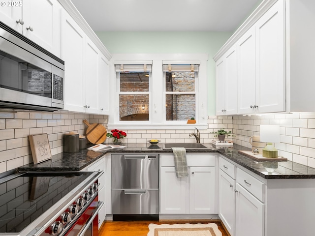2127 NW Irving St Unit 104, Portland, OR 97210 - kitchen featuring appliances with stainless steel finishes, a sink, white cabinets, and dark stone counters
