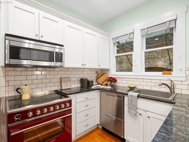2127 NW Irving St Unit 104, Portland, OR 97210 - kitchen with appliances with stainless steel finishes, white cabinetry, decorative backsplash, dark stone countertops, and a sink