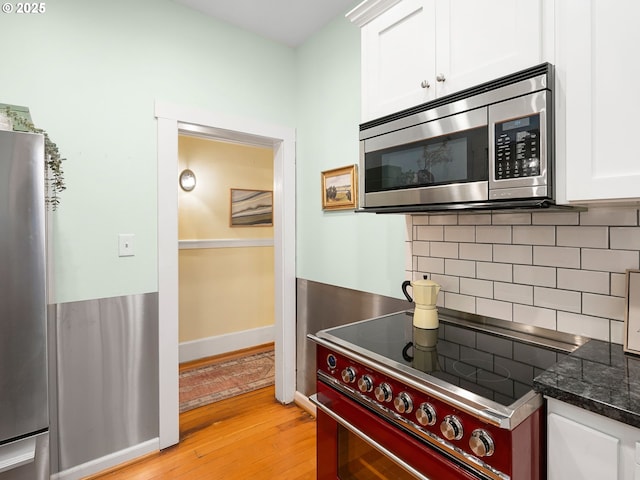 2127 NW Irving St Unit 104, Portland, OR 97210 - kitchen with appliances with stainless steel finishes, light wood finished floors, white cabinetry, tasteful backsplash, and dark stone counters