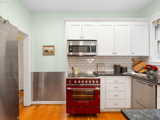 2127 NW Irving St Unit 104, Portland, OR 97210 - kitchen with stainless steel appliances, white cabinets, light wood finished floors, and backsplash