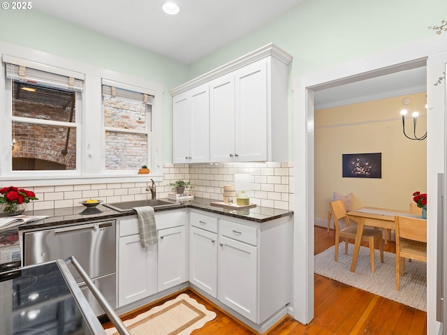 2127 NW Irving St Unit 104, Portland, OR 97210 - kitchen featuring tasteful backsplash, white cabinets, light wood-style flooring, stainless steel dishwasher, and ornamental molding