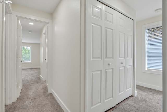 corridor featuring light colored carpet and baseboards
