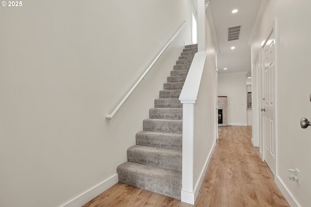 stairs featuring wood finished floors, a stone fireplace, baseboards, and recessed lighting