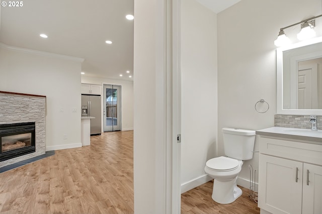 bathroom with wood finished floors, toilet, a stone fireplace, crown molding, and vanity