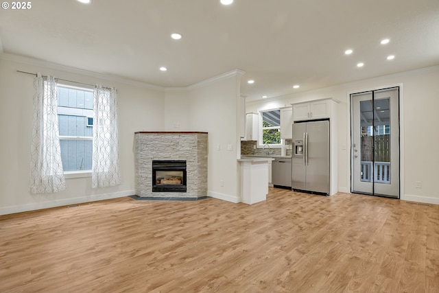 unfurnished living room with ornamental molding, light wood finished floors, baseboards, recessed lighting, and a fireplace