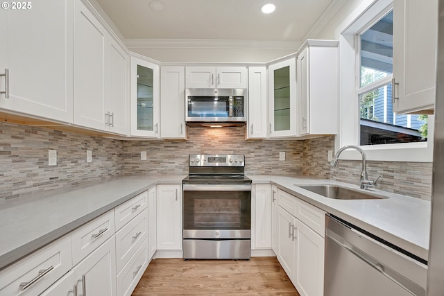 kitchen featuring stainless steel appliances, a sink, white cabinets, light countertops, and ornamental molding