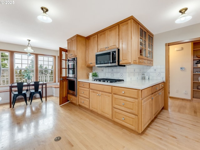 kitchen featuring decorative light fixtures, light hardwood / wood-style flooring, decorative backsplash, light stone countertops, and appliances with stainless steel finishes