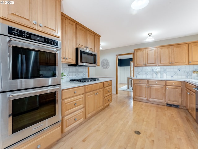 kitchen featuring stainless steel appliances, light wood-type flooring, and tasteful backsplash