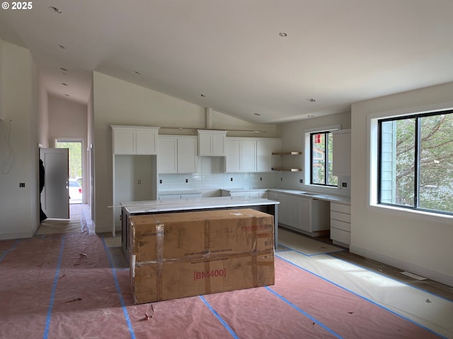 559 Meadows Dr, Manzanita, OR 97130 - kitchen featuring tasteful backsplash, white cabinetry, vaulted ceiling, a kitchen island, and baseboards