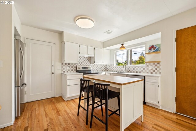5515 SE 62nd Ave, Portland, OR 97206 - kitchen with stainless steel appliances, decorative backsplash, white cabinets, light wood finished floors, and a kitchen bar