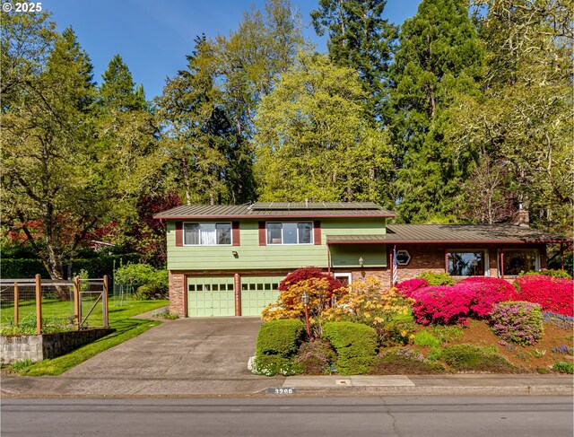 3290 Fillmore St, Eugene, OR 97405 - split level home featuring a garage, driveway, roof mounted solar panels, brick siding, and a metal roof