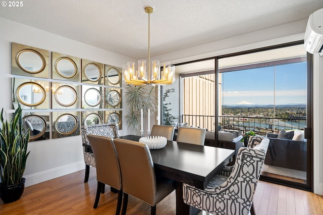 dining area featuring a wall mounted air conditioner, wood-type flooring, a notable chandelier, a water view, and a textured ceiling