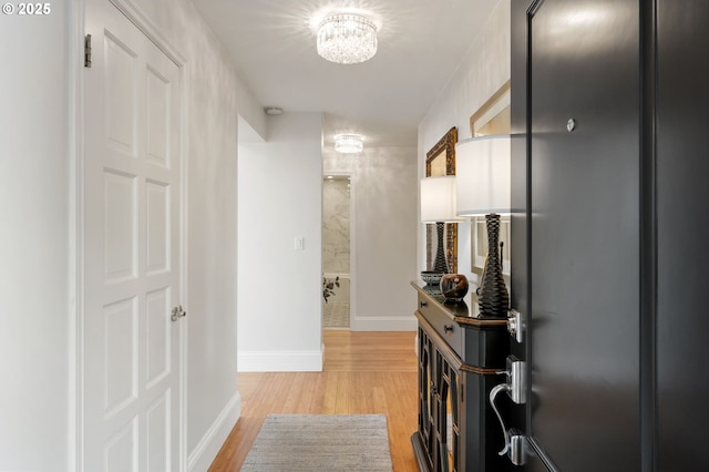 hallway featuring light wood finished floors, a notable chandelier, and baseboards