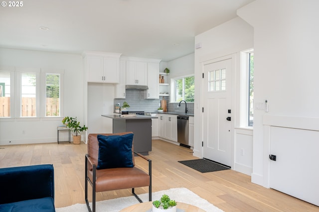 5827 NE 16th Ave, Portland, OR 97211 - kitchen with under cabinet range hood, light wood-style flooring, stainless steel dishwasher, white cabinets, and backsplash