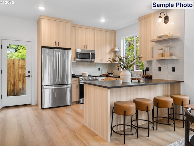 kitchen featuring dark countertops, light wood finished floors, light brown cabinets, stainless steel appliances, and a peninsula