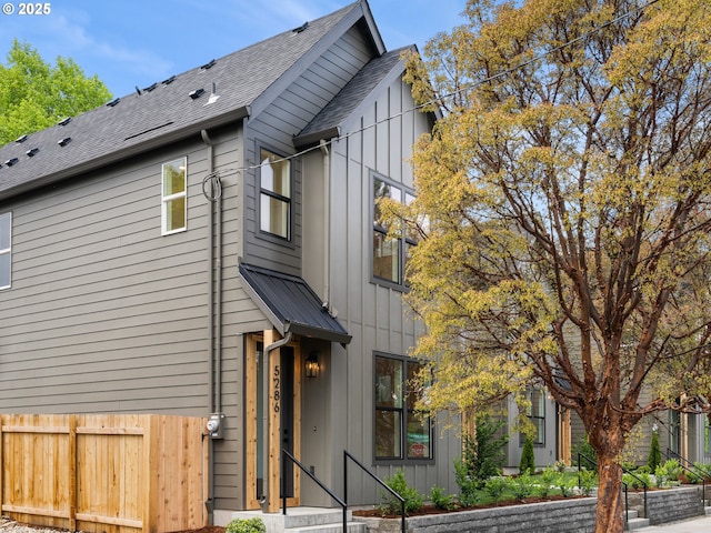 view of property exterior with a shingled roof, board and batten siding, and fence