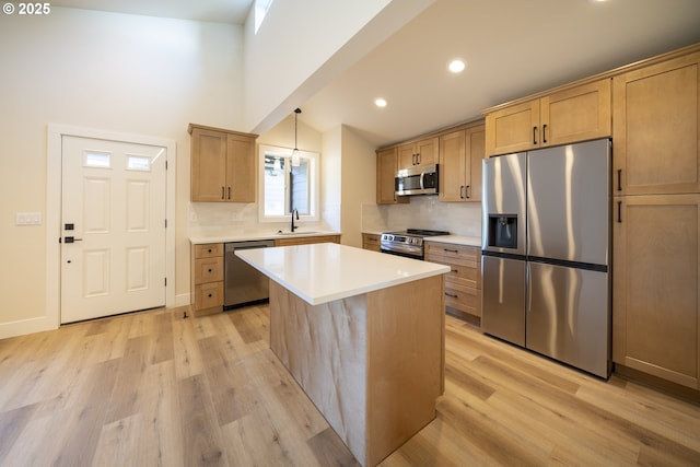 kitchen with a kitchen island, appliances with stainless steel finishes, light countertops, light wood-type flooring, and pendant lighting