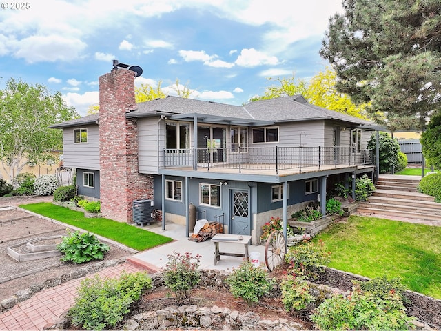back of property with a shingled roof, a chimney, cooling unit, a patio area, and a lawn