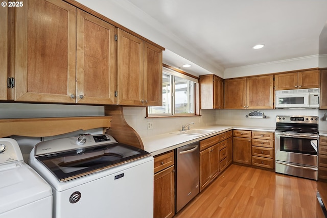 kitchen with brown cabinets, light countertops, stainless steel appliances, light wood-type flooring, and washer and clothes dryer