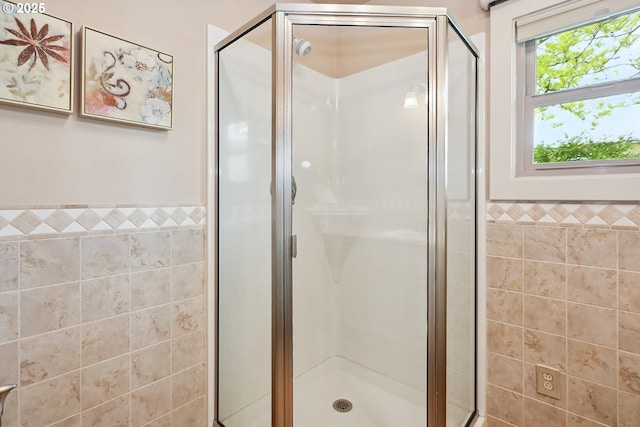 bathroom with a wainscoted wall, a stall shower, and tile walls