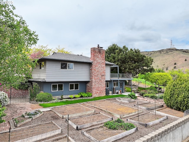 rear view of house with a balcony, a mountain view, a vegetable garden, and a chimney