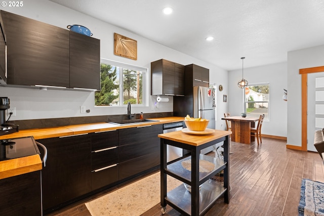 kitchen featuring modern cabinets, a sink, wood finished floors, stainless steel appliances, and wooden counters