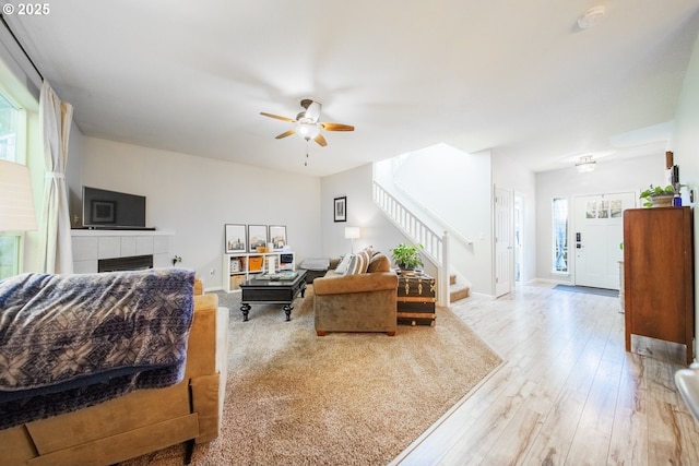 living room with a tile fireplace, ceiling fan, and light wood-type flooring