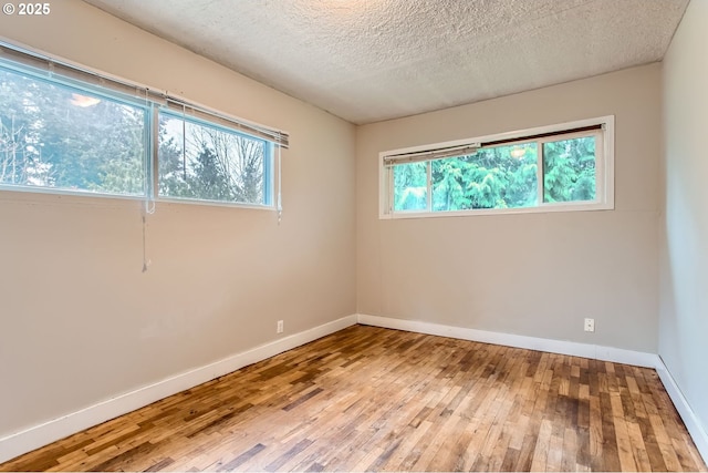 spare room with a textured ceiling, baseboards, and hardwood / wood-style flooring