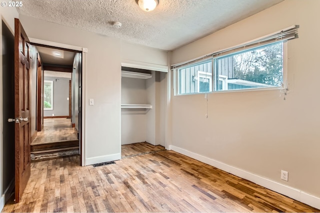 unfurnished bedroom with visible vents, a textured ceiling, wood finished floors, a closet, and baseboards