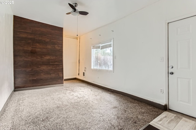 empty room featuring baseboards, wooden walls, ceiling fan, and an accent wall