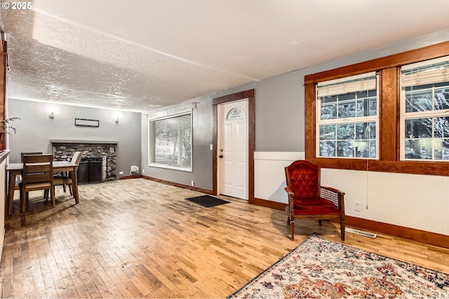 entryway featuring baseboards, a textured ceiling, a stone fireplace, and hardwood / wood-style floors