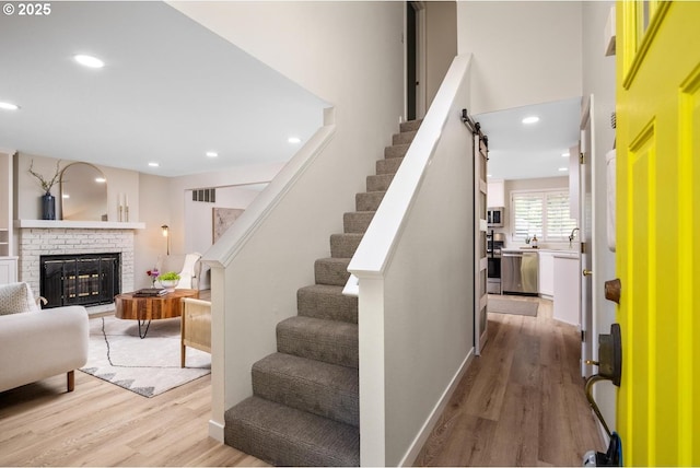 staircase with wood finished floors, recessed lighting, and a brick fireplace