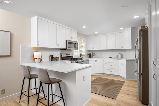 kitchen featuring stainless steel appliances, a peninsula, white cabinetry, backsplash, and light countertops