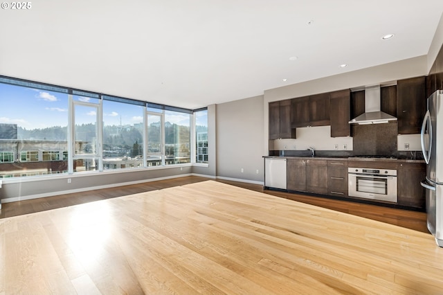 kitchen with wall chimney range hood, hardwood / wood-style flooring, sink, dark brown cabinets, and stainless steel appliances