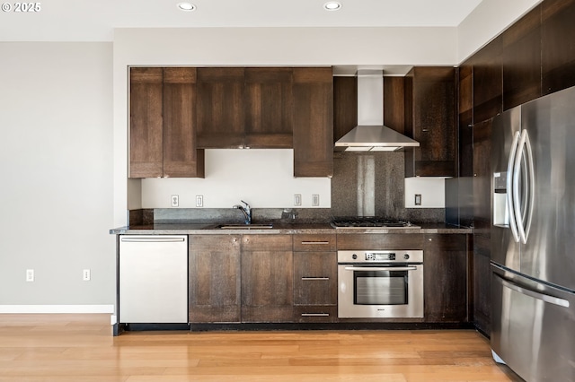 kitchen featuring wall chimney exhaust hood, sink, dark brown cabinets, light wood-type flooring, and stainless steel appliances