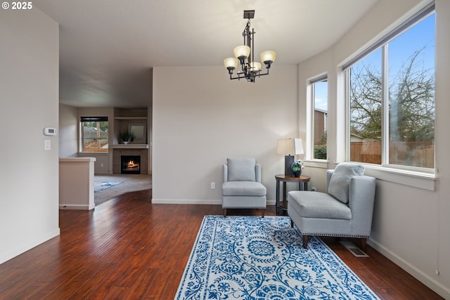 living area with dark wood-style floors, a warm lit fireplace, baseboards, and an inviting chandelier