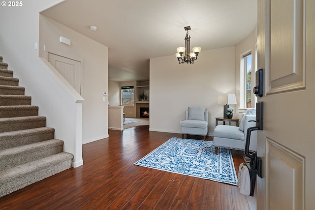 living area featuring dark wood finished floors, an inviting chandelier, a warm lit fireplace, baseboards, and stairs